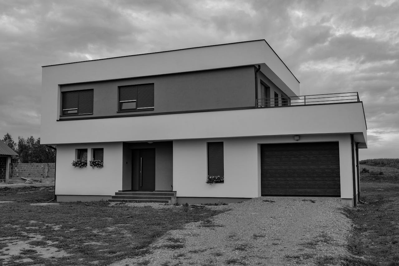 gallery-2 Grayscale photo of a modern two-story house with a garage, showcasing contemporary architecture.