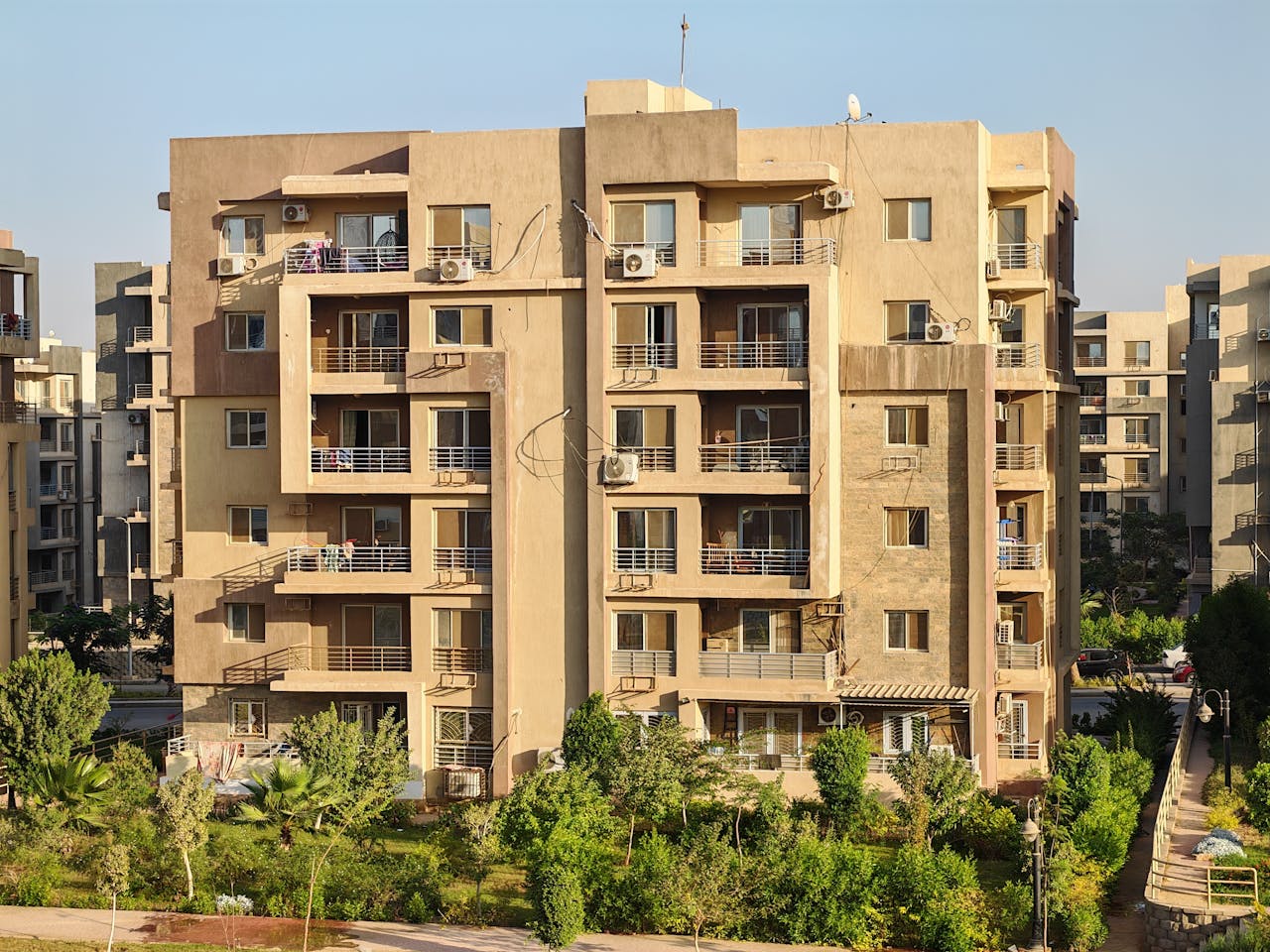 services-01 A modern apartment complex with greenery in a sunny urban environment.